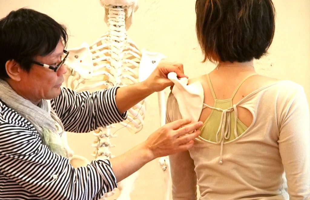 ヨガ講師(内田かつのり)が生徒さんの肩甲骨に模型を体に当てて形を確認している様子