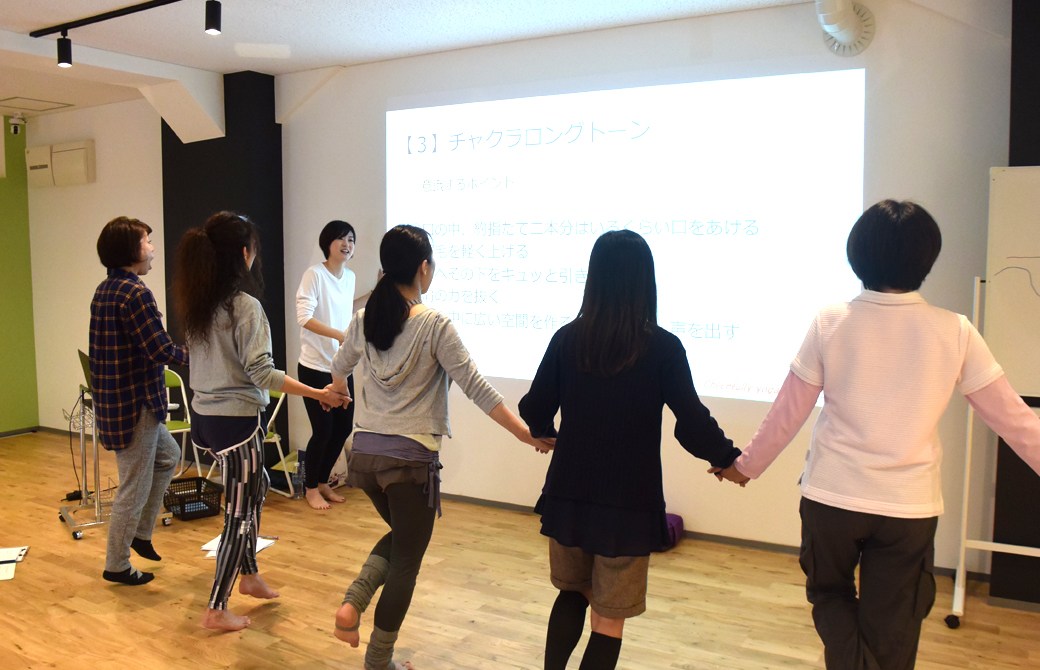 声・話し方をテーマにしたスキルアップヨガ講座:実践編 声・話し方をテーマにしたスキルアップヨガ講座:実践編 高橋淳子先生が生徒さんにアドバイスをしている様子 高橋淳子先生の声かけ、はないちもんめのように手をつないで横一列になった生徒さんが壁に向かって発声している様子